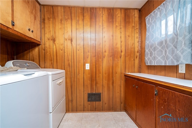 laundry room with washing machine and clothes dryer, wooden walls, light tile patterned flooring, and cabinets