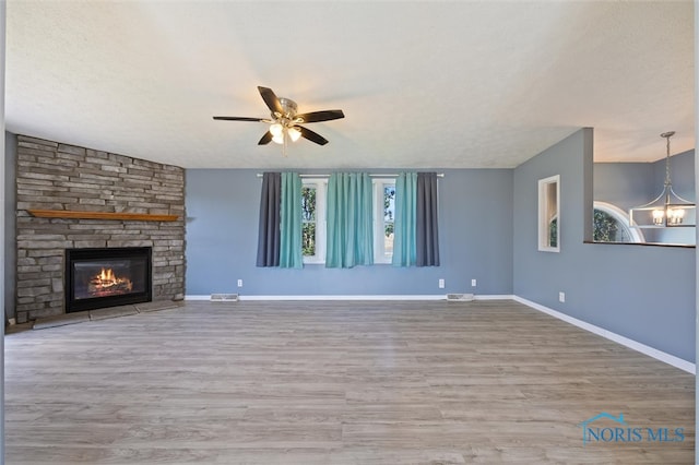 unfurnished living room with a fireplace, wood-type flooring, ceiling fan with notable chandelier, and a textured ceiling