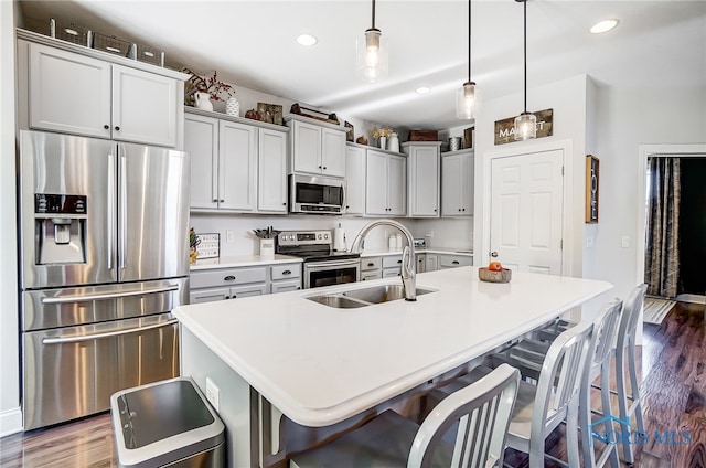 kitchen featuring stainless steel appliances, hanging light fixtures, an island with sink, and dark hardwood / wood-style flooring