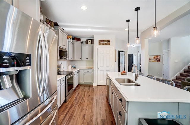 kitchen with appliances with stainless steel finishes, pendant lighting, sink, and an island with sink