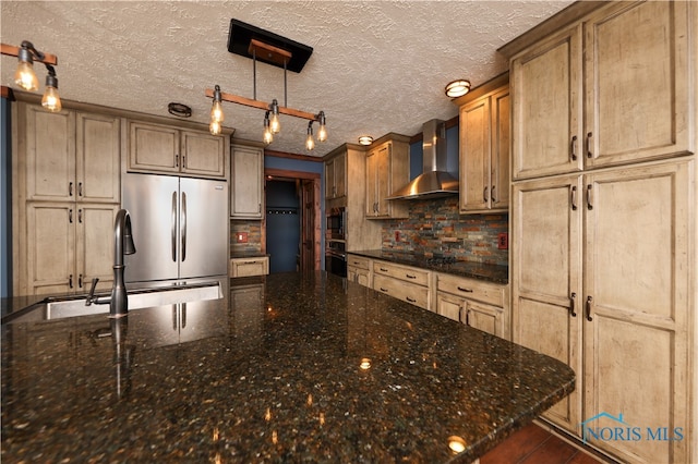 kitchen featuring stainless steel appliances, dark stone countertops, wall chimney range hood, hanging light fixtures, and a textured ceiling