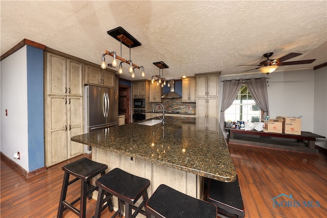 kitchen with appliances with stainless steel finishes, wall chimney range hood, a textured ceiling, and dark hardwood / wood-style flooring