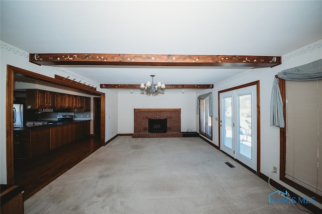 unfurnished living room with light colored carpet, beamed ceiling, a fireplace, and a chandelier