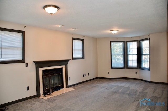 unfurnished living room with a healthy amount of sunlight, carpet flooring, and a tiled fireplace