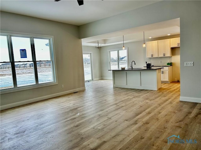 kitchen featuring ceiling fan with notable chandelier, sink, white cabinets, hanging light fixtures, and light wood-type flooring