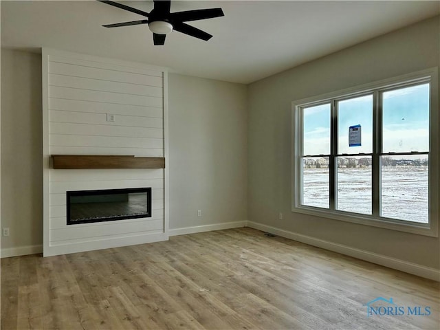 unfurnished living room featuring a large fireplace, ceiling fan, and light wood-type flooring