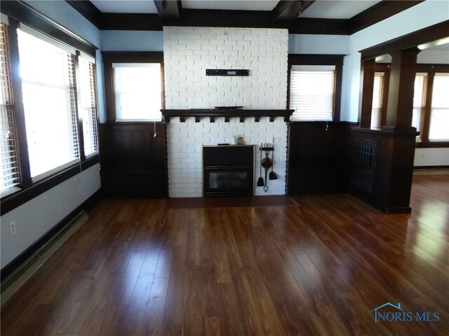 unfurnished living room with dark wood-type flooring, plenty of natural light, and decorative columns