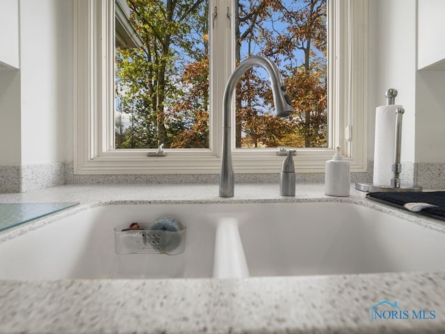 room details featuring white cabinets, light stone countertops, and sink