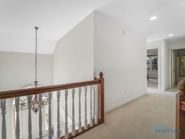 hall featuring a notable chandelier, vaulted ceiling, and carpet floors