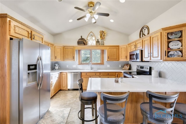 kitchen with kitchen peninsula, lofted ceiling, appliances with stainless steel finishes, a kitchen bar, and sink