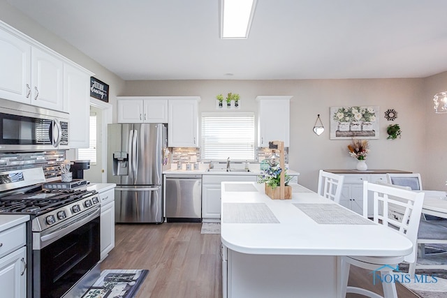 kitchen with white cabinets, stainless steel appliances, light wood-type flooring, and decorative backsplash