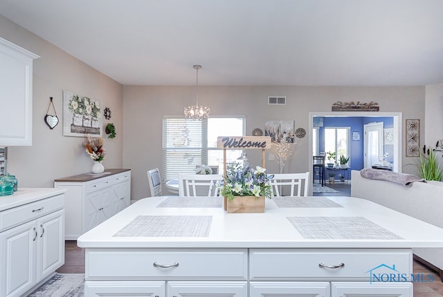 kitchen with a kitchen island, dark hardwood / wood-style flooring, pendant lighting, a notable chandelier, and white cabinetry