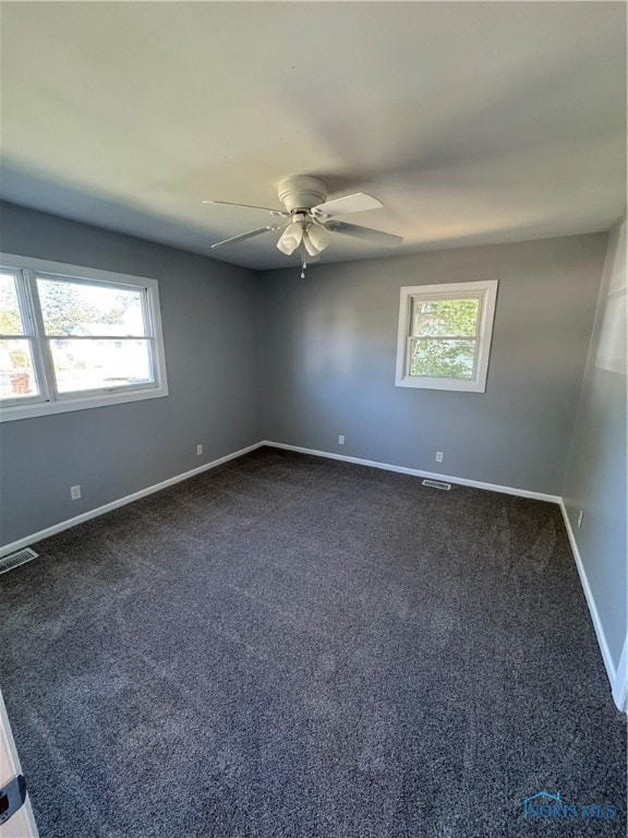 empty room with plenty of natural light, dark colored carpet, and ceiling fan