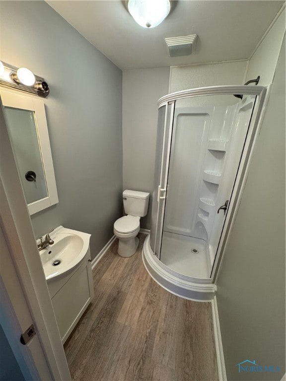 bathroom with hardwood / wood-style floors, a shower with shower door, vanity, and toilet