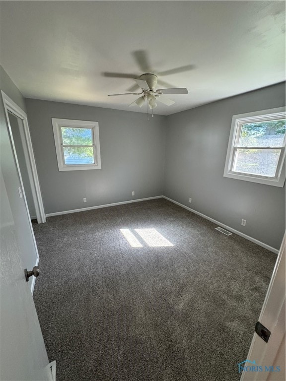 spare room featuring dark colored carpet and ceiling fan