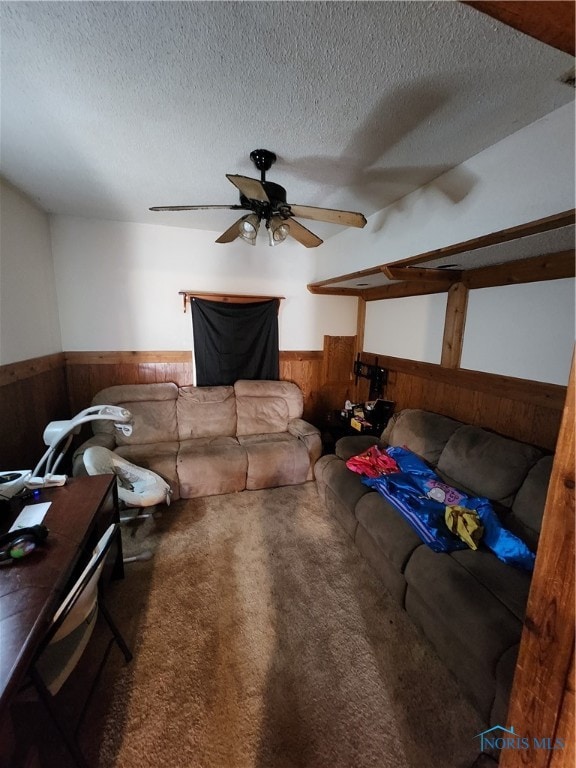 carpeted living room featuring wooden walls, ceiling fan, and a textured ceiling