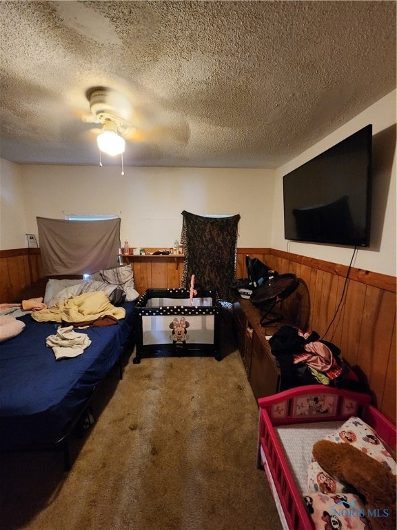 carpeted bedroom featuring ceiling fan, a textured ceiling, and wooden walls