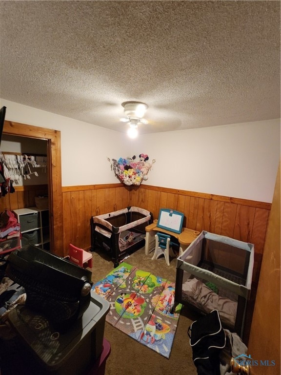 carpeted bedroom with wooden walls, ceiling fan, and a textured ceiling