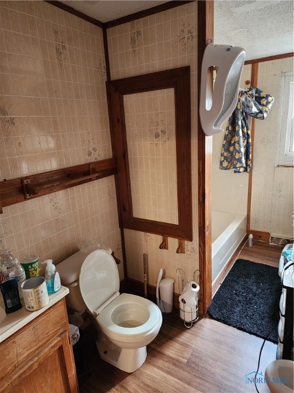 bathroom with tile walls, a bath, hardwood / wood-style floors, and toilet