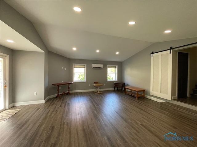 unfurnished living room with a wall mounted air conditioner, a barn door, vaulted ceiling, and dark hardwood / wood-style floors