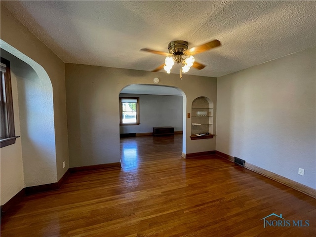 spare room with ceiling fan, a textured ceiling, dark hardwood / wood-style floors, and built in shelves