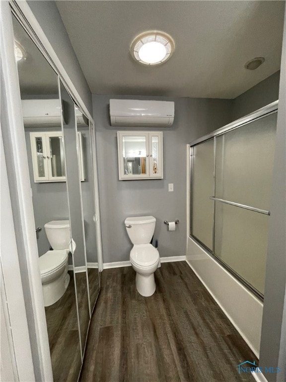 bathroom featuring combined bath / shower with glass door, wood-type flooring, a wall unit AC, and toilet