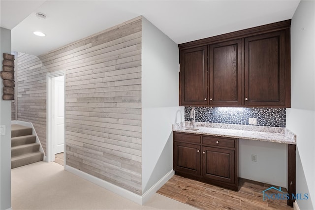 bar with light hardwood / wood-style flooring, dark brown cabinetry, built in desk, and light stone counters