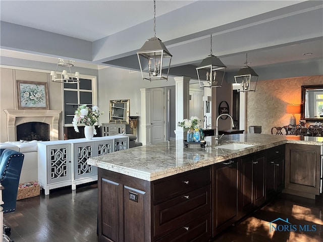 kitchen featuring light stone countertops, sink, dark brown cabinets, dark hardwood / wood-style flooring, and decorative light fixtures