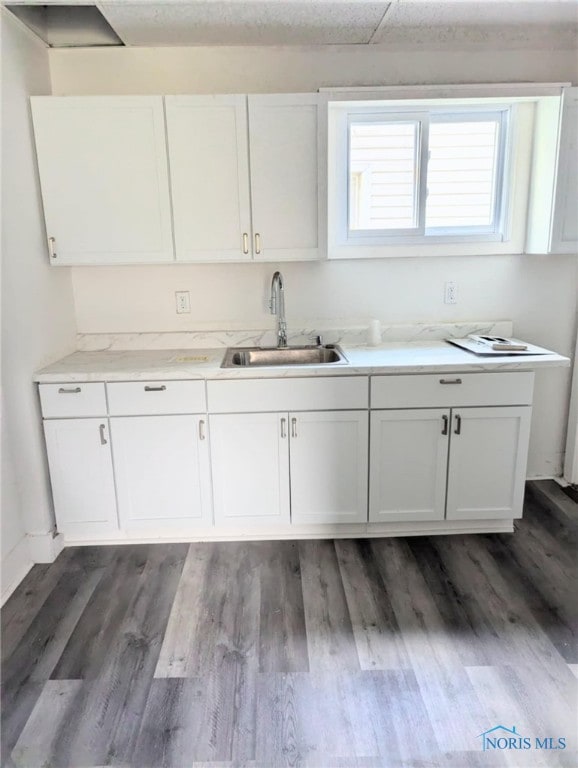 kitchen with light countertops, white cabinetry, a sink, and wood finished floors