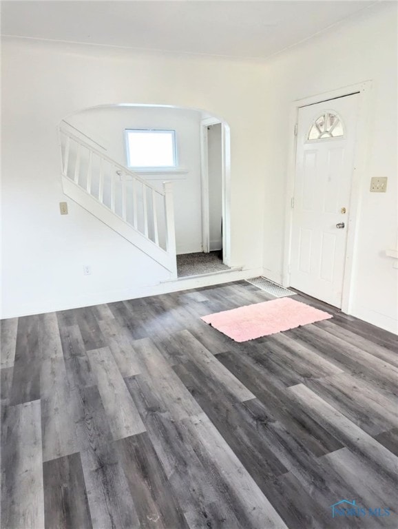 entrance foyer featuring arched walkways, wood finished floors, and stairs