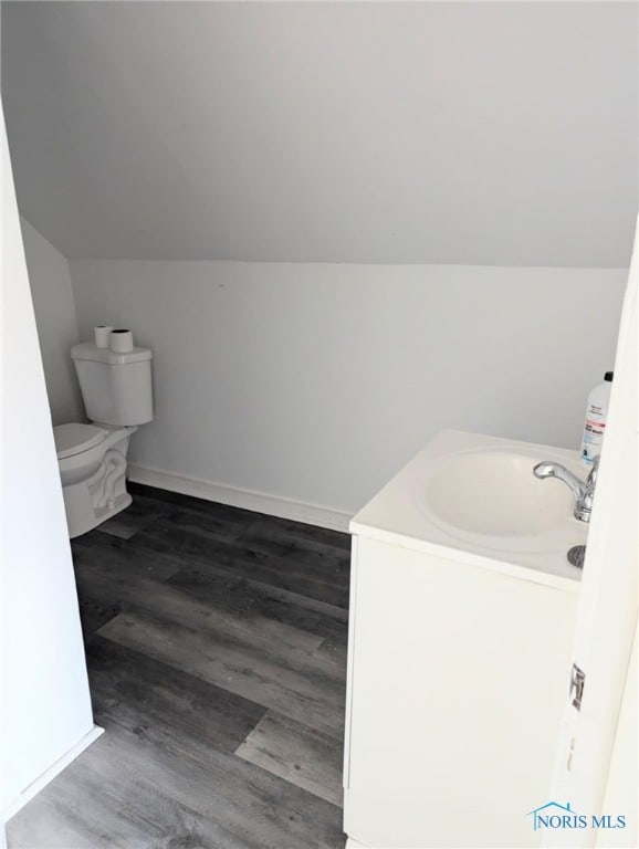 bathroom featuring wood-type flooring, toilet, vanity, and vaulted ceiling