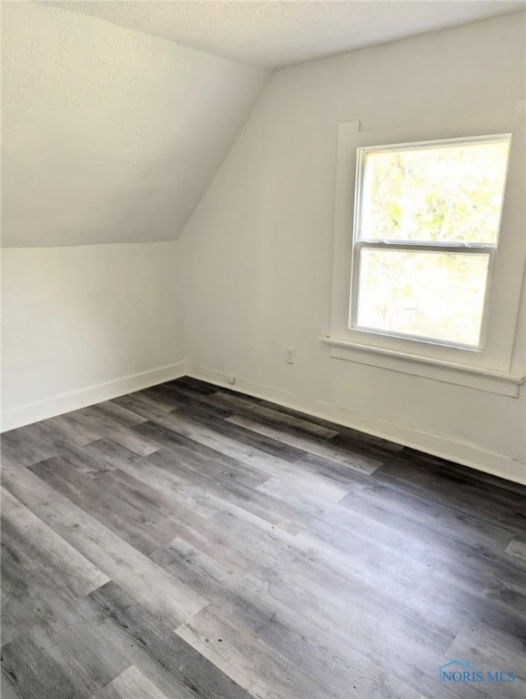 additional living space featuring a textured ceiling, baseboards, dark wood-style floors, and vaulted ceiling