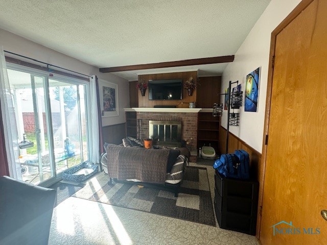 carpeted living room with a brick fireplace, beamed ceiling, wood walls, and a textured ceiling