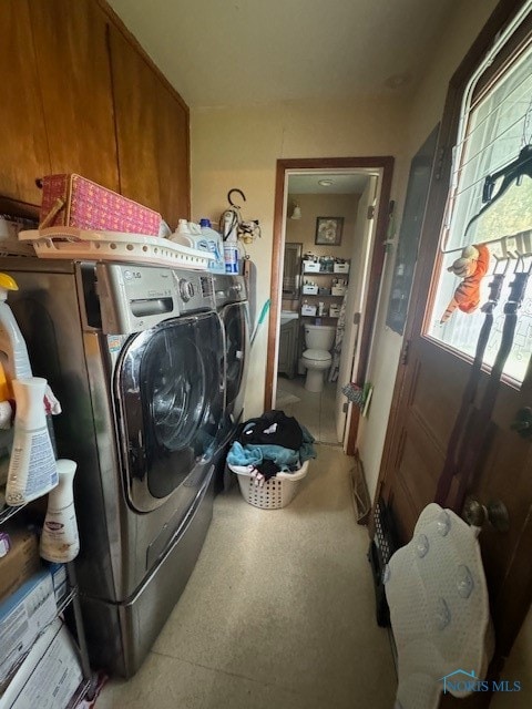 clothes washing area featuring washing machine and clothes dryer, cabinets, and a healthy amount of sunlight