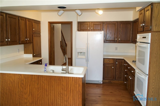 kitchen with sink, kitchen peninsula, dark hardwood / wood-style floors, and white appliances