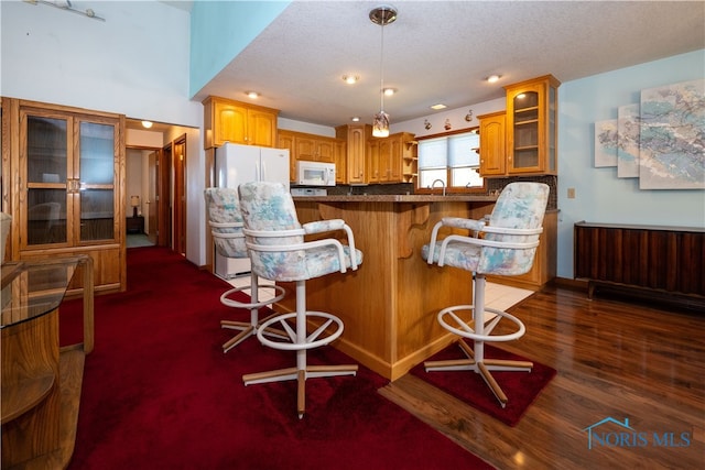 kitchen featuring kitchen peninsula, a breakfast bar, a textured ceiling, dark hardwood / wood-style floors, and white appliances