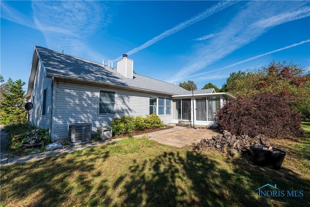 back of property featuring central air condition unit, a sunroom, a lawn, and a patio area