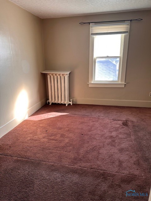 unfurnished room with a textured ceiling, radiator heating unit, and carpet flooring