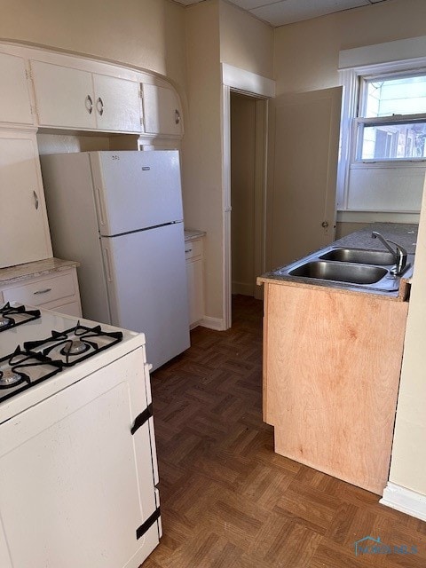 kitchen with white appliances, white cabinetry, sink, and dark parquet flooring