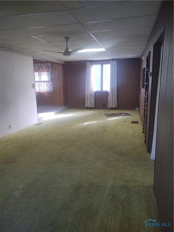 empty room with a paneled ceiling, ceiling fan, wood walls, and carpet