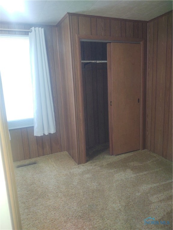 unfurnished bedroom featuring wood walls, a closet, and carpet