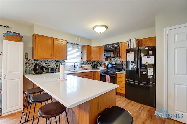 kitchen with sink, kitchen peninsula, black appliances, a breakfast bar, and light wood-type flooring