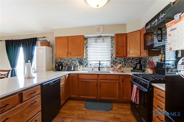 kitchen with tasteful backsplash, light hardwood / wood-style floors, black appliances, and sink