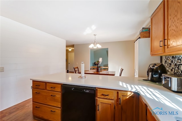 kitchen with an inviting chandelier, black dishwasher, kitchen peninsula, backsplash, and hardwood / wood-style flooring