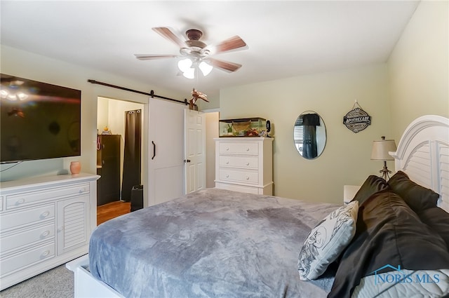 carpeted bedroom with a barn door and ceiling fan