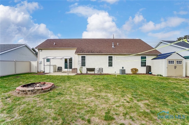 rear view of property with a storage unit, a fire pit, cooling unit, a lawn, and a patio area