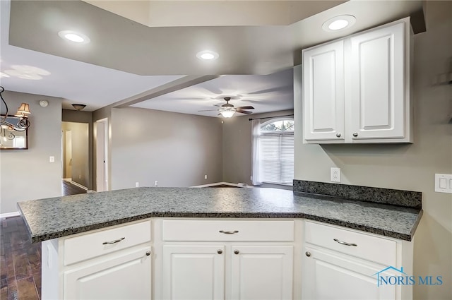 kitchen with kitchen peninsula, ceiling fan, white cabinets, dark stone countertops, and dark hardwood / wood-style floors