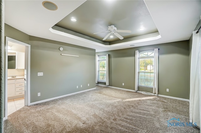 carpeted empty room with ceiling fan and a raised ceiling