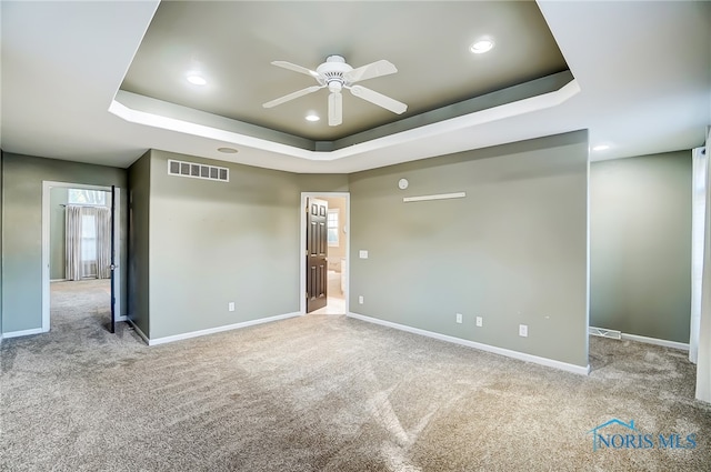 carpeted spare room with ceiling fan and a raised ceiling