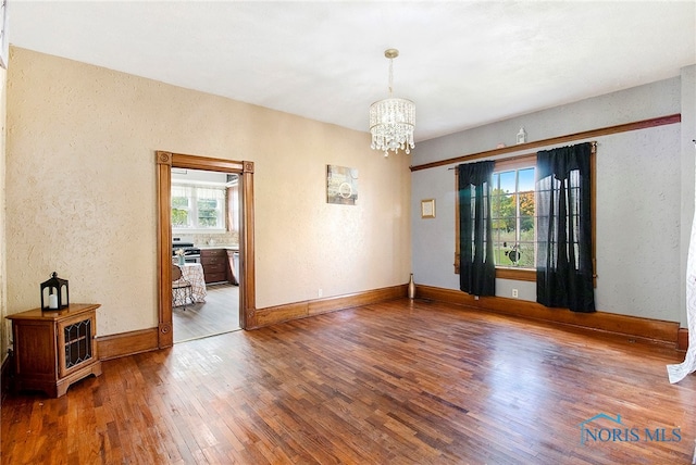 spare room with hardwood / wood-style flooring and an inviting chandelier